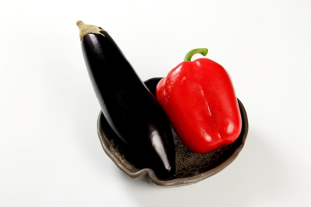 Eggplant and red organic peppers in a clay plate on a white background