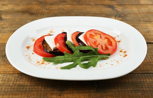 Eggplant salad with tomato and feta cheese on plate on wooden background