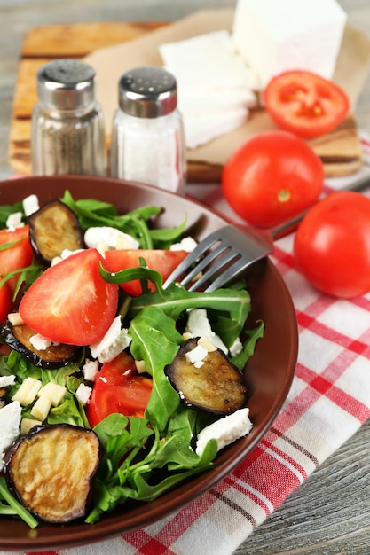 Eggplant salad with tomatoes arugula and feta cheese on napkin on color wooden background