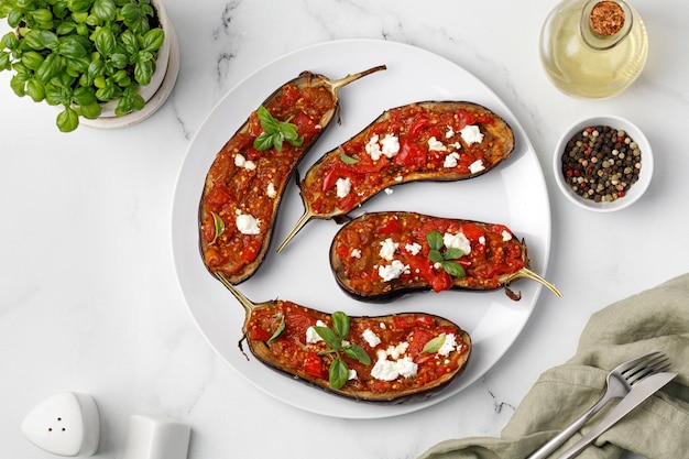 Eggplants Baked grilled halves of eggplants stuffed with red sauce chopped tomatoes on white plate