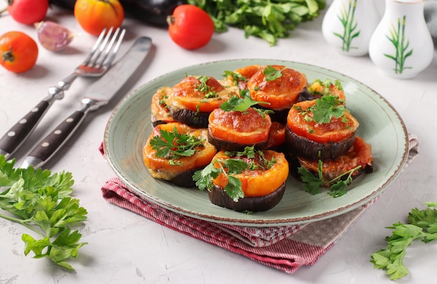 Melanzane e pomodori al forno con formaggio e aglio serviti su piatto su sfondo grigio