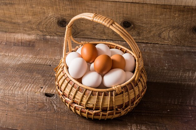 Photo eggs in a basket over old wooden brown background.