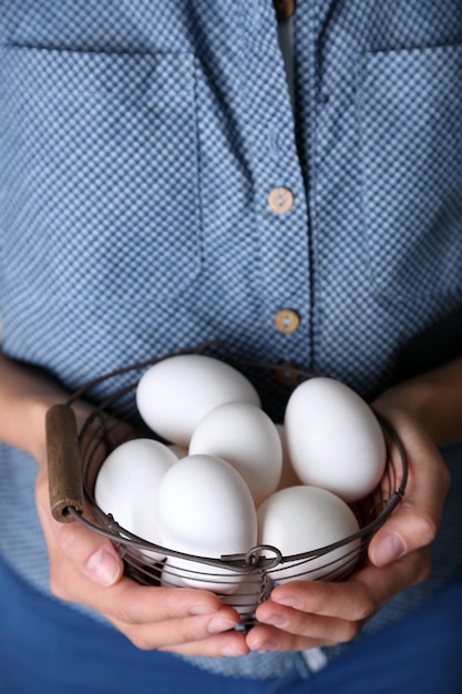 Eggs in basket in women hands on wooden background