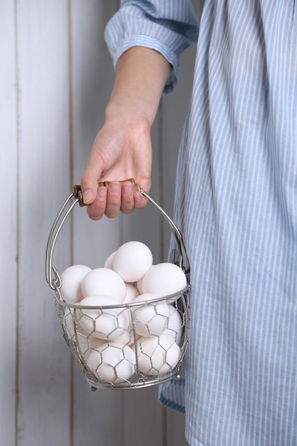 Eggs in basket in women hands on wooden background