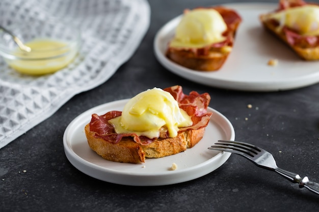 Uova benedict: pane tostato inglese, prosciutto crudo, uova in camicia con salsa olandese e limone su grigio