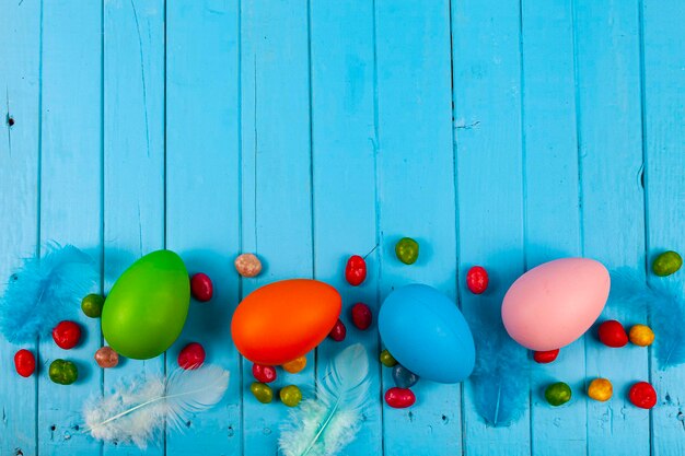 Eggs, candies and feathers on a blue wooden background, place for your text. Easter still life.