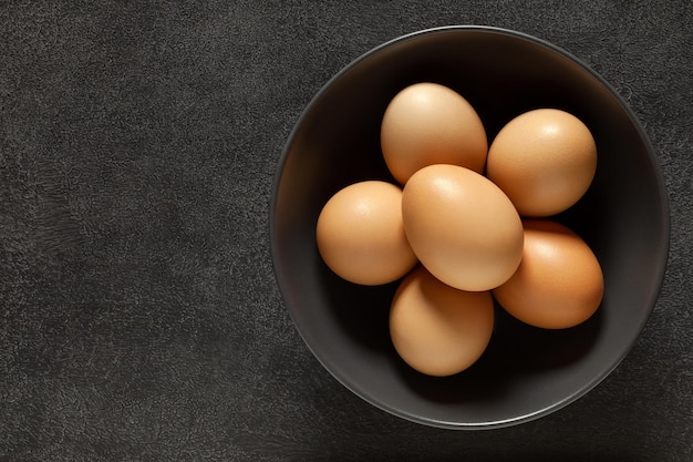 Eggs chicken whole beige in bowl on dark background top view space to copy text
