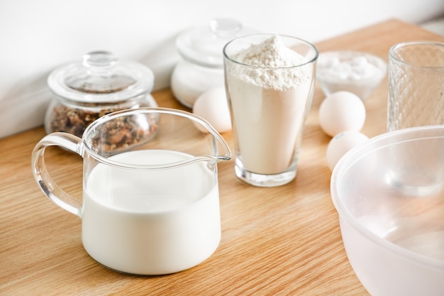 Eggs, flour a decanter with milk on the table and a whisk