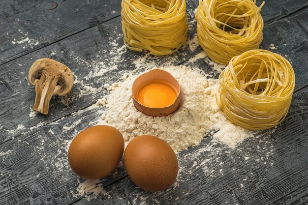 Uova, farina e pasta sotto forma di nido su un tavolo di legno. ingredienti per fare la pasta.