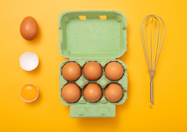 Eggs in green tray with yolkwhisk and shell on yellow background top view
