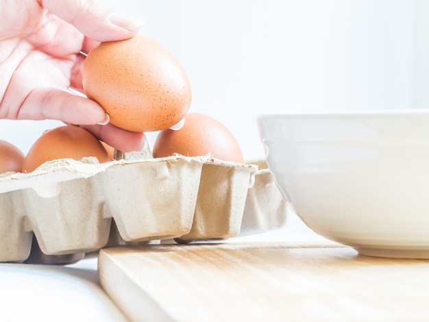 Eggs in paper tray with woman hand and white bowl for preparing meal