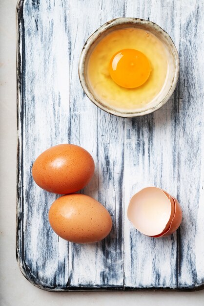 Eggs over a rustic cutting board. Cracked egg in tiny ceramic bowl. Top View. Flat Lay.