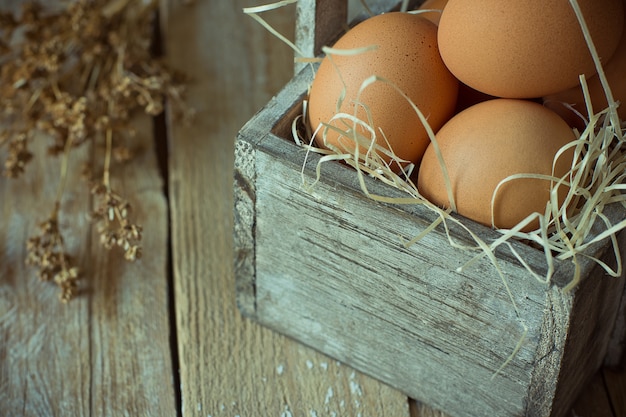 Foto uova su paglia in scatola di legno d'annata con il piccolo mazzo di fiori asciutti beige. composizione in stile rustico