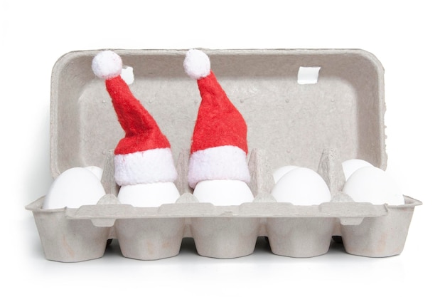 Eggs in toy christmas hats in a cardboard packing on a white background