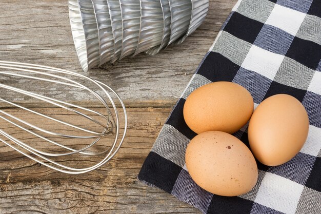 Eggs, whisk and baking pans. On wooden table.