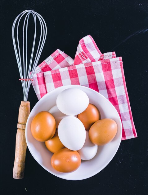 Eggs and whisk on a black surface