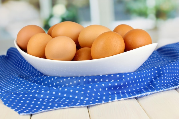 Eggs in white bowl on wooden table on window background