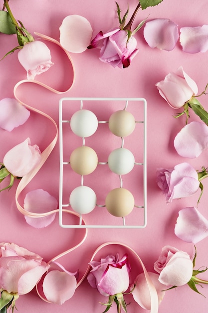 Eggs in white ceramic holder and flowers on pink background. Top view.