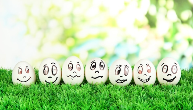 Eggs with funny faces on grass on bright background