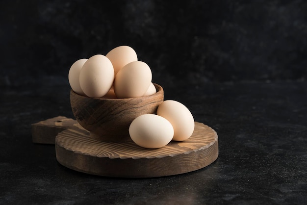 Eggs on wood board in wooden bowl dark background