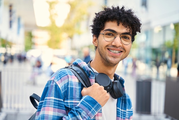 Egyptian student wearing headphones smiling to the camera while standing with backpack. Education