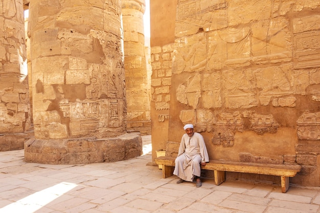 An Egyptian in traditional clothes sits on a bench near the Egyptian columns. Luxor. Egypt