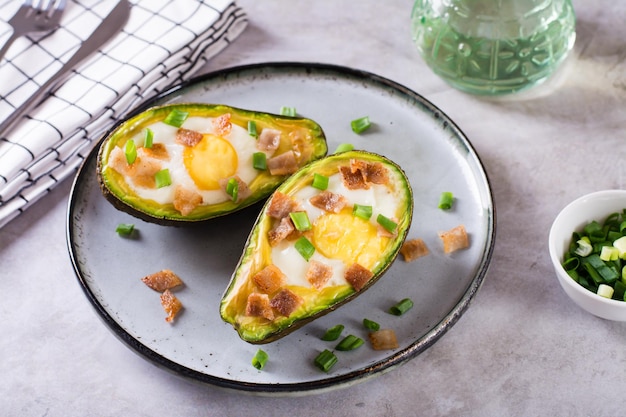 Ei gebakken in avocado bestrooid met spek en kruiden op een bord