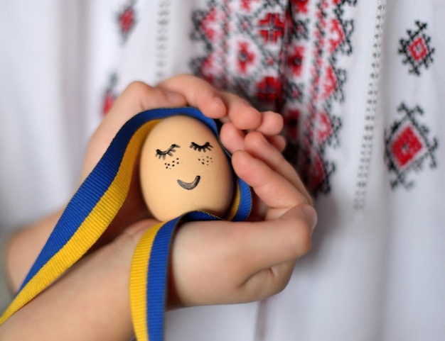 Ei met geschilderd gezicht en Oekraïens lint en Oekraïens ornament op onscherpe achtergrond