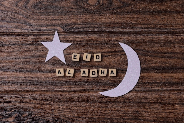 이슬람 축제 축하를 위해 나무 배경에 달과 별이 있는 Eid Al Adha 단어입니다.