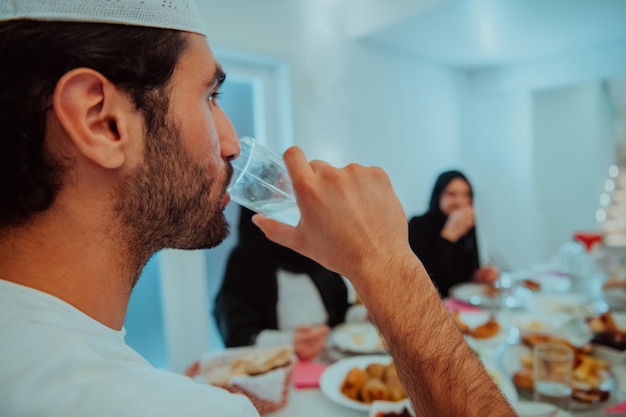 Мусульманская семья Ид Мубарак обедает ифтаром, пьет воду, чтобы разбить пир. Еда традиционной еды во время праздника Рамадан дома. Исламская халяльная еда и питье в современном западном Исле