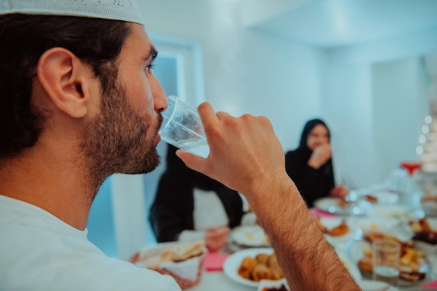 Eid Mubarak Muslim family having Iftar dinner drinking water to break feast. Eating traditional food during Ramadan feasting month at home. The Islamic Halal Eating and Drinking at modern western Isla