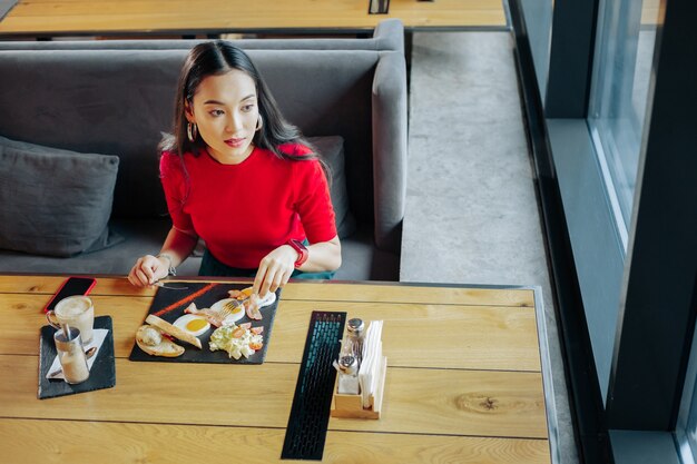 Eieren en koffie. Donkerharige stijlvolle vrouw die eieren eet en koffie drinkt bij het ontbijt