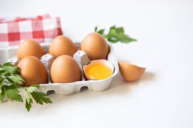 Eieren in karton met peterselie en rode doek op witte tafel