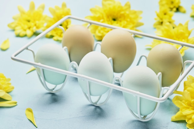 Eieren in witmetalen houder en bloemen op blauwe tafel. bovenaanzicht