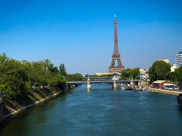 Eiffel tower by river against blue sky