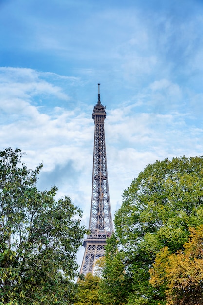 Eiffel Tower among the lush green trees against a bright blue cloudy sky. Vertical.