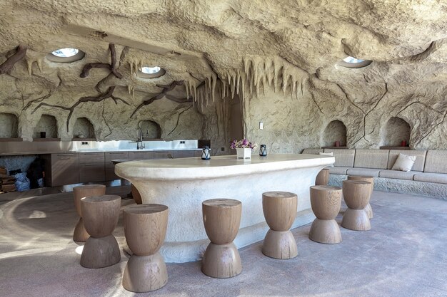Eigenaardige patio uitgerust in kunstmatige rotsachtige grot met grote ovale marmeren tafel en houten stoelen, zachte loungebank en keukenkasten