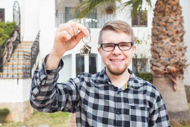 Eigendom, onroerend goed, onroerend goed en huurder concept - portret van een vrolijke jonge man met sleutel van nieuw huis.