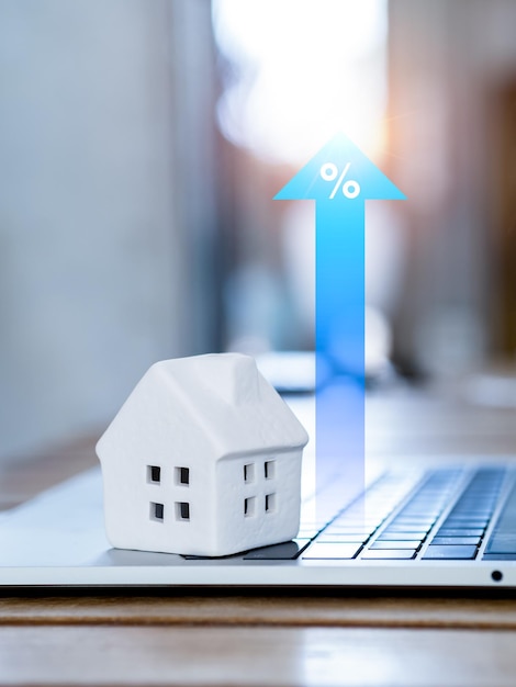 Eigendomswaarde onroerend goed investeringen hypotheek en huisbelasting concepten Percentagepictogram op grote blauwe stijgende pijl omhoog in de buurt van wit miniatuurhuis op laptopcomputer op houten tafel verticale stijl