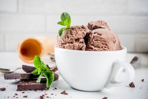 Eigengemaakt chocoladeroomijs dat met verse munt, donkere chocolade en wafelroomijskegels, witte marmeren achtergrondexemplaarruimte wordt gediend