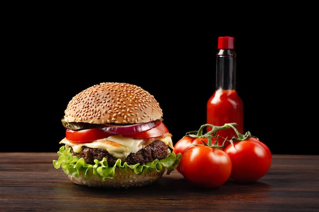 Eigengemaakt hamburgerclose-up met rundvlees, tomaten, sla, kaas en sausfles op houten lijst. fast food