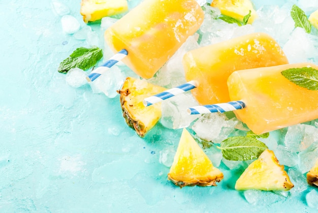 Eigengemaakte Ananasijslollys op Ijs met verse Ananasplakken en munt op lichtblauwe achtergrond