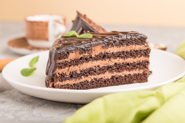 Eigengemaakte chocoladecake met melkroom en een kop van koffie op een grijze concrete achtergrond. zijaanzicht, selectieve aandacht.