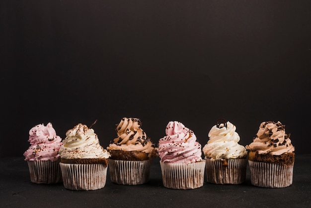 Foto eigengemaakte cupcakes op een rij op zwarte achtergrond