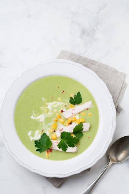 Eigengemaakte groene soeppuree van broccoli, avocado, kip en maïs met room in rustieke ceramische plaat op wit beton