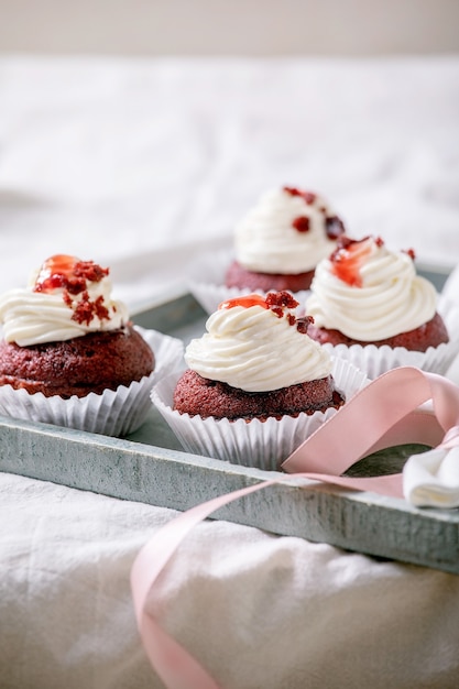 Eigengemaakte Rood fluweel cupcakes met slagroom op houten dienblad, wit servet met lint op witte linnen tafelkleed.