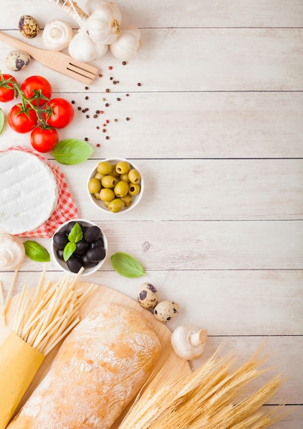 Eigengemaakte spaghettideegwaren met kwartelseieren met fles tomatensaus en kaas op houten achtergrond. Klassiek Italiaans dorpsvoedsel. Knoflook, champignons, zwarte en groene olijven, brood en tarwe