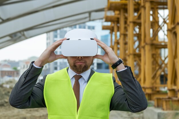 Eigentijdse aannemer in pak en vr-headset die rondkijkt op de bouwplaats