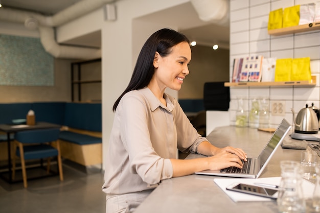 Eigentijdse jonge vrouwelijke eigenaar van café of restaurant aan het eind van de werkdag door laptop zitten en plan maken voor de volgende dag