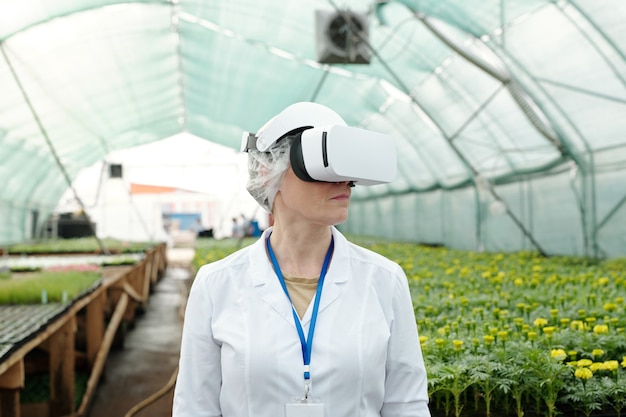 Eigentijdse vrouwelijke expert in d-headset die tegen groeiende zaailingen staat